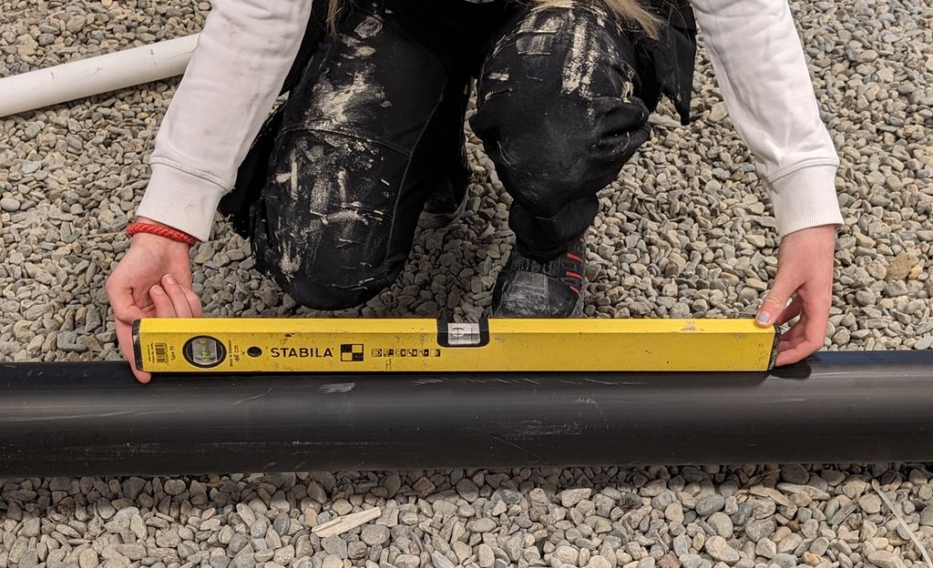 En person har lagt et vater ned på et avløpsrør og har lagt pekefingeren imellom vateret og røret i den lave enden av vateret. Foto.