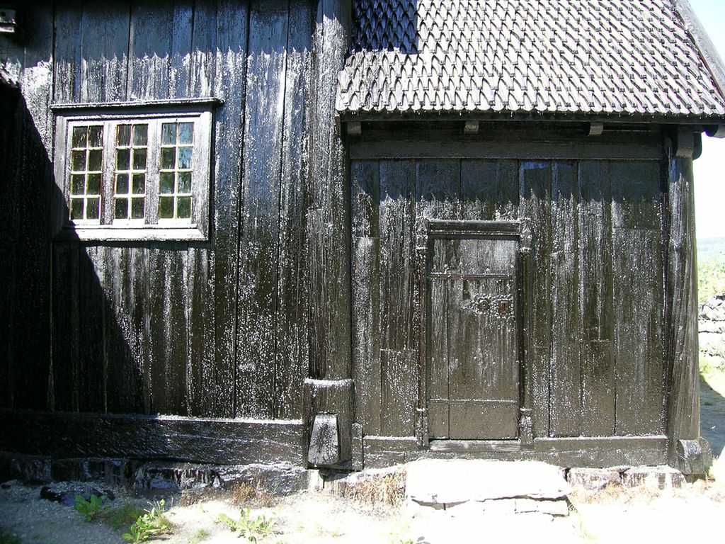 Ein vegg på ei kyrkje er måla med svart tjøremåling. Foto.