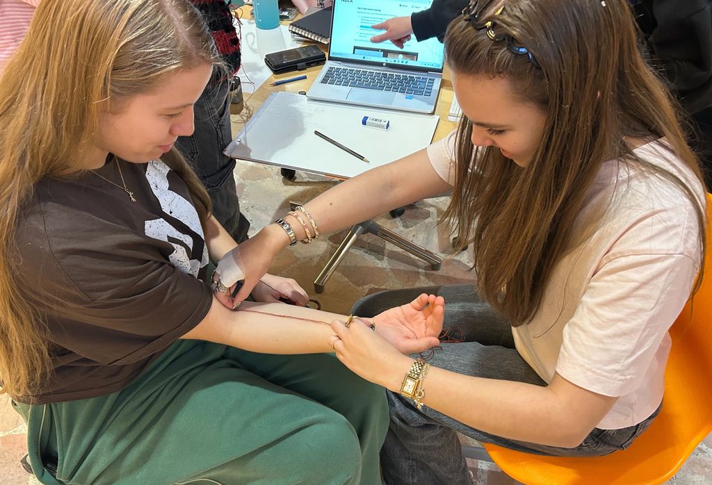 To jenter sit mot kvarandre. Den eine måler underarmen til den andre med ein hyssing. Foto.