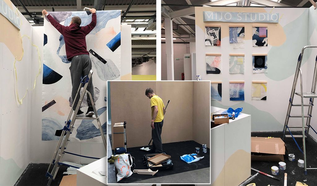 Bilete av klargjering og rigging av messestand. Ein mann står i ei gardintrapp og henger opp eit tekstiltrykk, ein annan målar veggane. Foto.