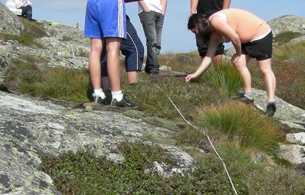 Ungdommer undersøker vegetasjon langs et tau som ligger på bakken. Foto.