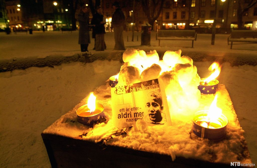 Avisutklipp med bilde av Benjamin Hermansen. Det står foran en varde laget av små snøballer med lys i midten. Rundt denne er det fire tente fakler. Foto.