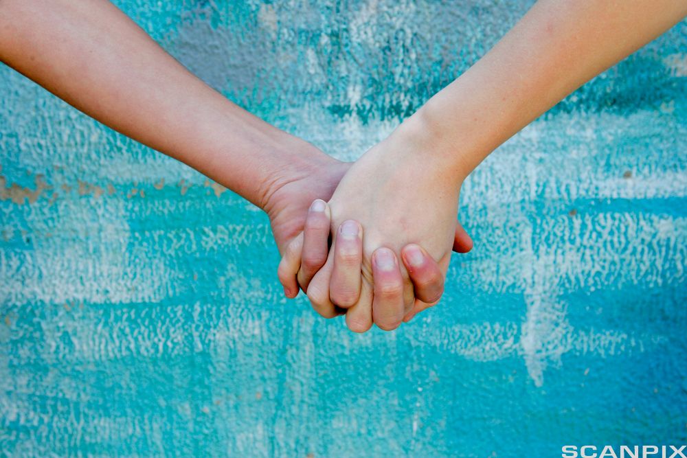 Two people holding hands against a textured blue and green background. Photo.