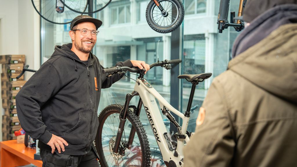 Sykkelselger står og snakker med en kunde ved siden av en utstilt elektrisk MTB-sykkel. Foto.