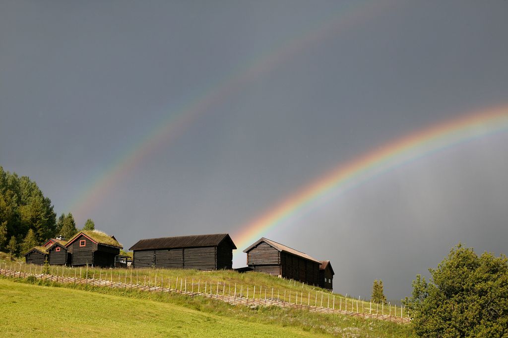 Regnbue og mørke skyer over en gammel fjellgård. Foto.