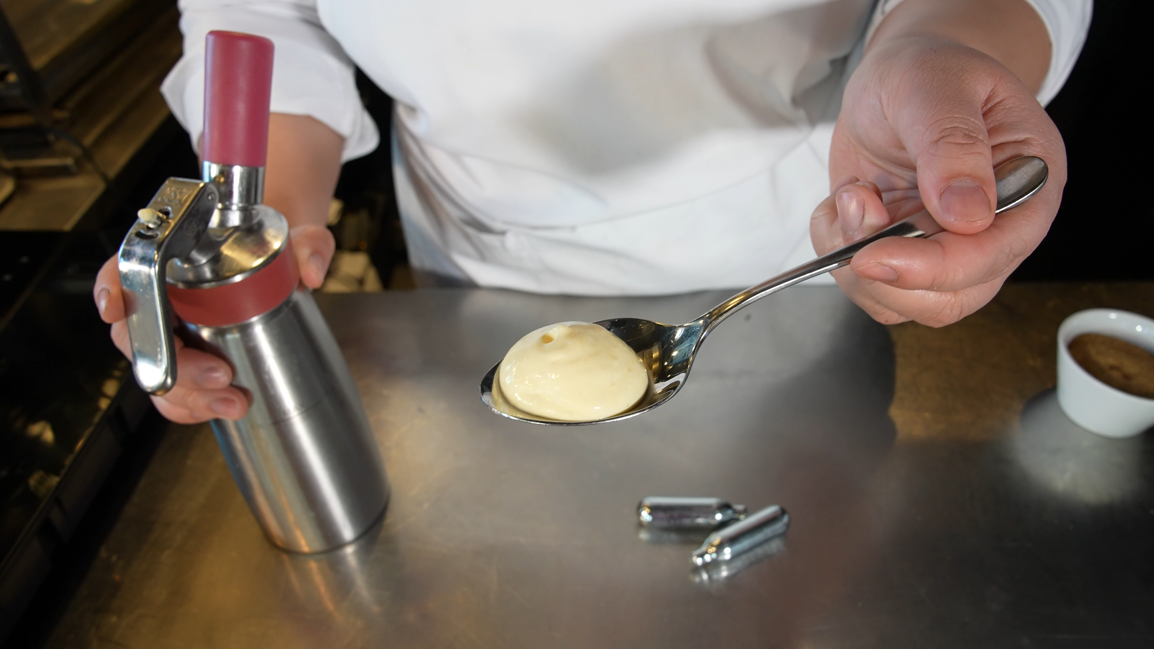 Hollandés på espumaflaske som er sprøytet ut i en serveringsskje. Foto.