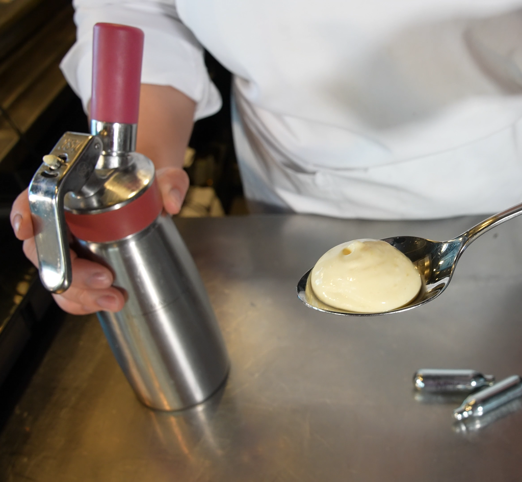 Hollandés på espumaflaske som er sprøytet ut i en serveringsskje. Foto.