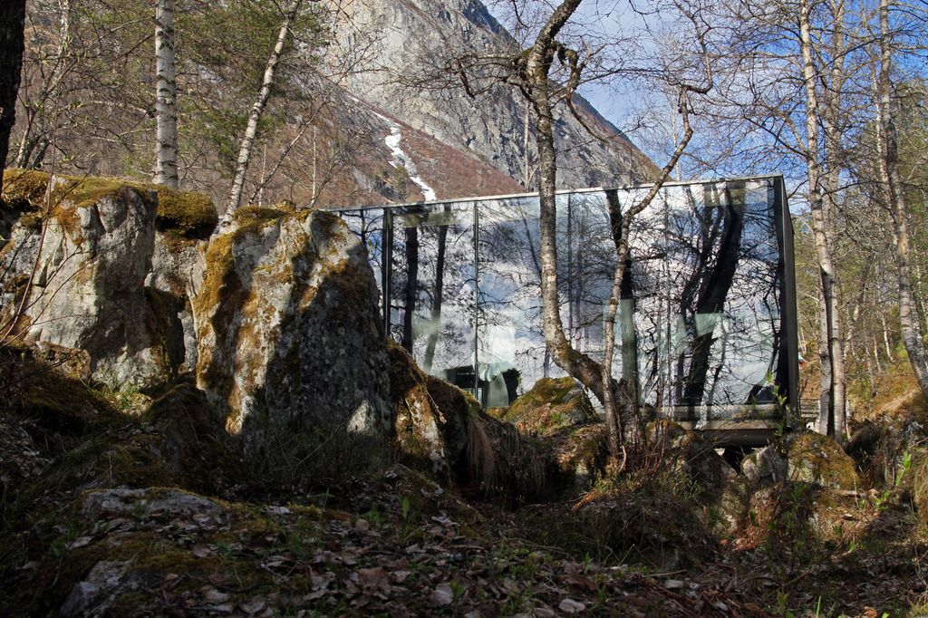 En liten bygningsenhet er plassert forsiktig inn i naturen mellom fjellknauser og trær. Foto.