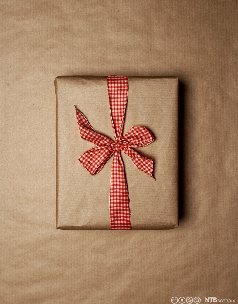 Gift wrapped in brown paper. It has a red and white bow. Photo.