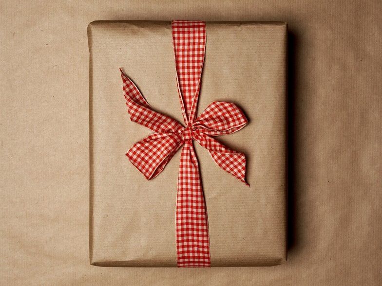 Gift wrapped in brown paper. It has a red and white bow. Photo.