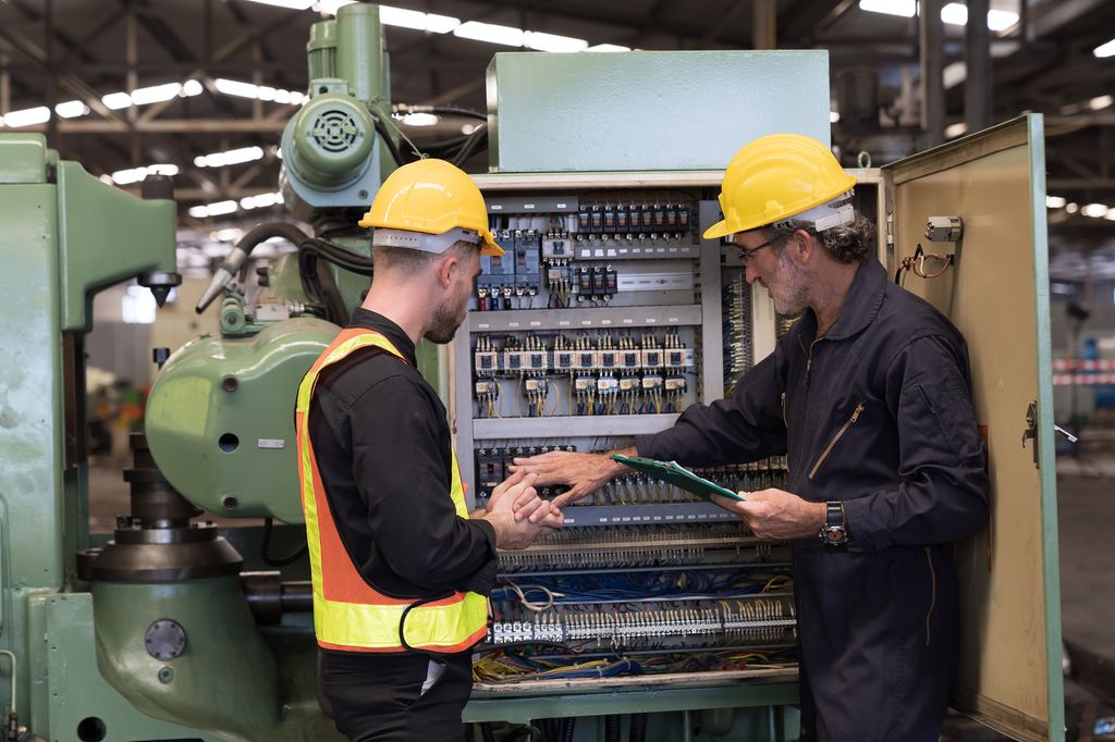 To elektrikere som sjekker det elektriske systemet til CNC-maskinen på en fabrikk. Foto.