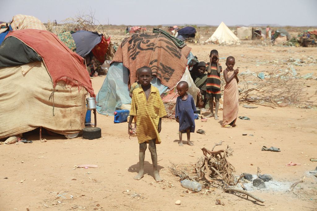 Barn står utenfor provisoriske telt i et tørt og karrig landskap. Foto.