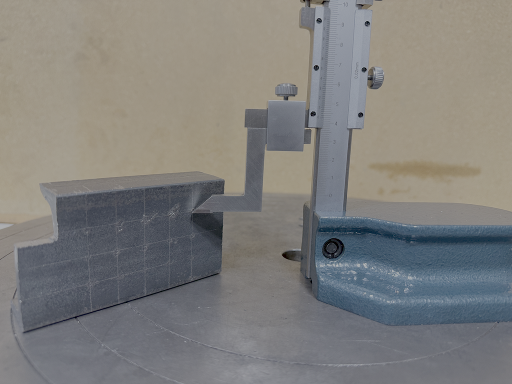 Måleverktøy stående på ei metallflate. Målespissen berører ei merka flate på et arbeidsstykke. Foto.