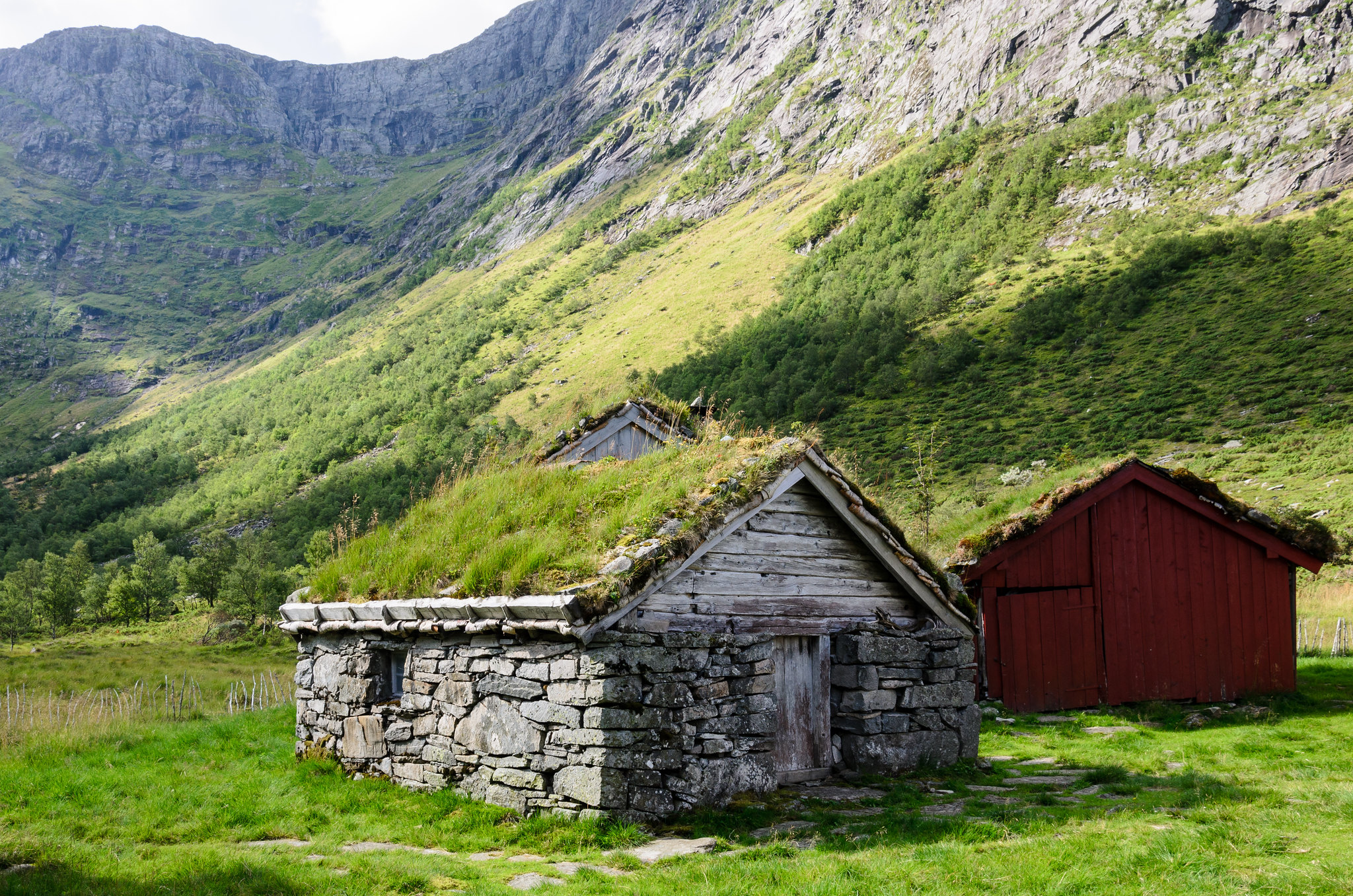 Eit gammalt steinhus med grastak på ein støl i ein dal. Foto. 