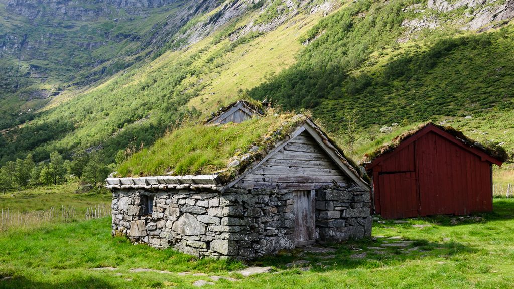 Eit gammalt steinhus med grastak på ein støl i ein dal. Foto.