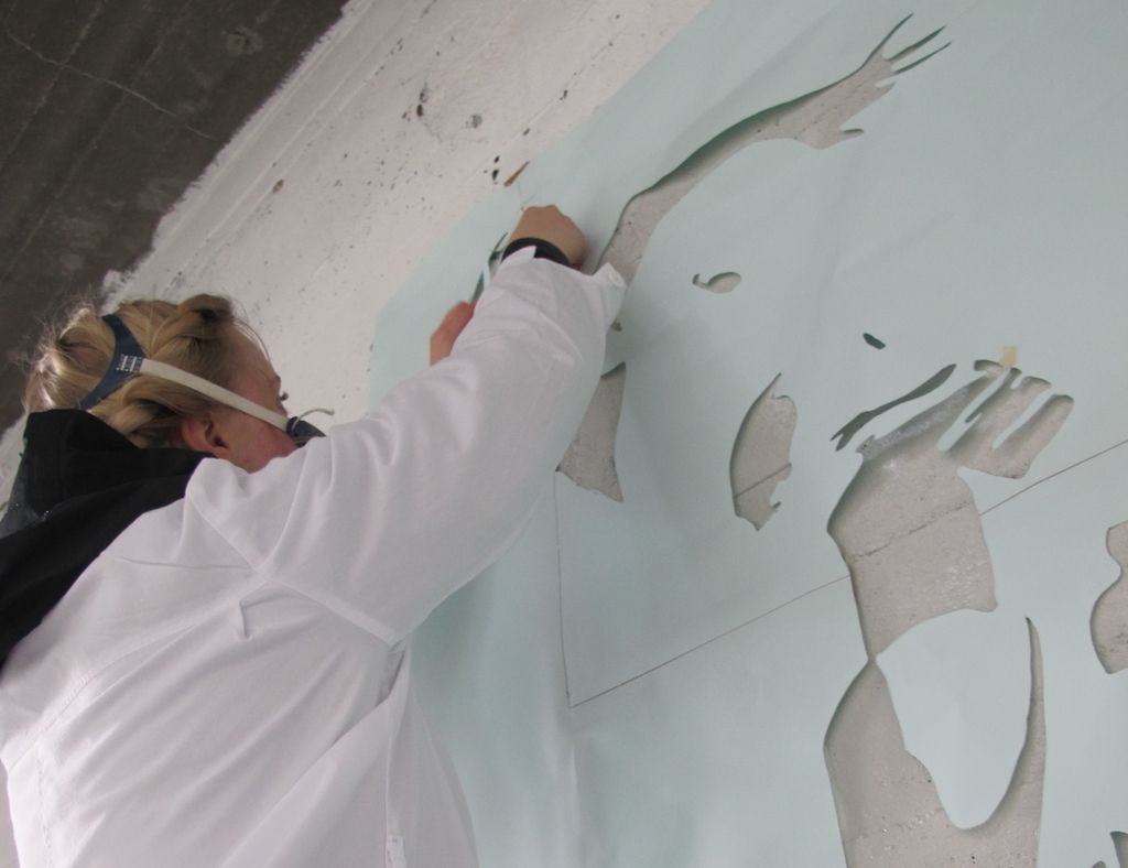 Jente jobber med en sjablong på en murvegg. Foto.