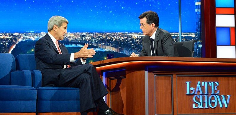Secretary John Kerry makes an appearance on The Late Show with Stephen Colbert. The two men are sitting on either side of a desk, in deep conversation.