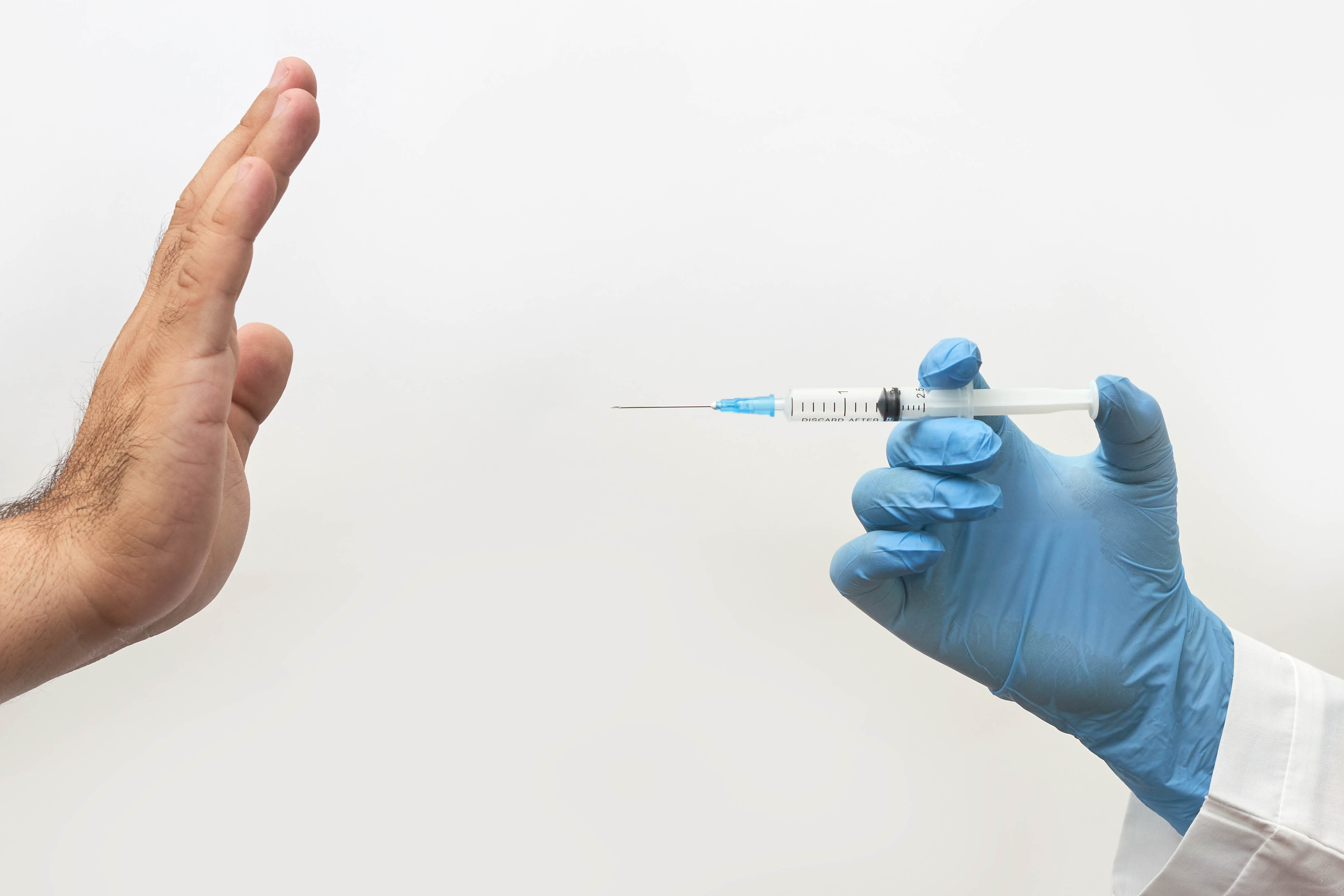 Two hands are showing: one is pointing a syringe towards the other hand. The other hand is declining the vaccine. Photo.