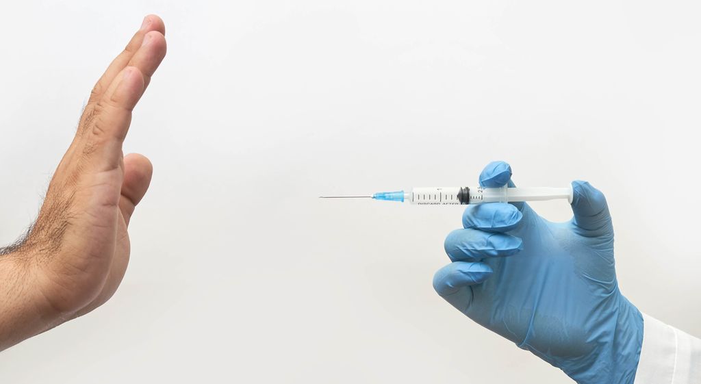 Two hands are showing: one is pointing a syringe towards the other hand. The other hand is declining the vaccine. Photo.
