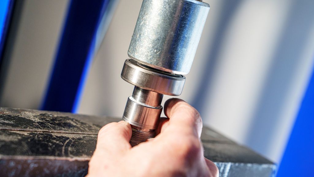 Hånd som holder to sylindriske deler. Foto.