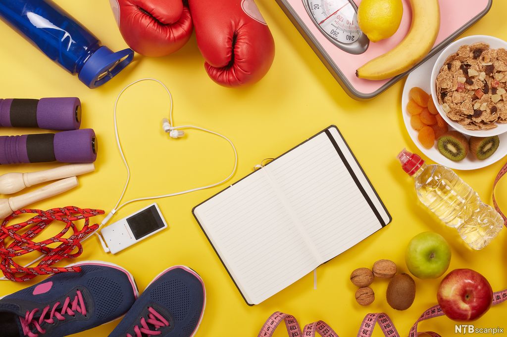Mobil og notisblokk omringa av treningsutstyr og mat. Foto.