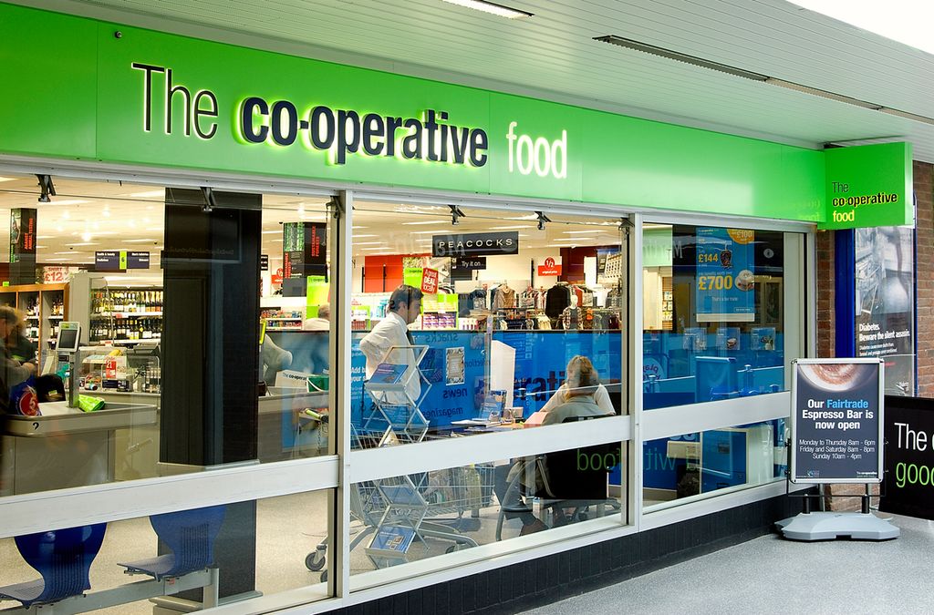 Inngangen til en coop-butikk i et engelsktalende land. På et grønt felt over vinduene står det The co-operative food. Foto.