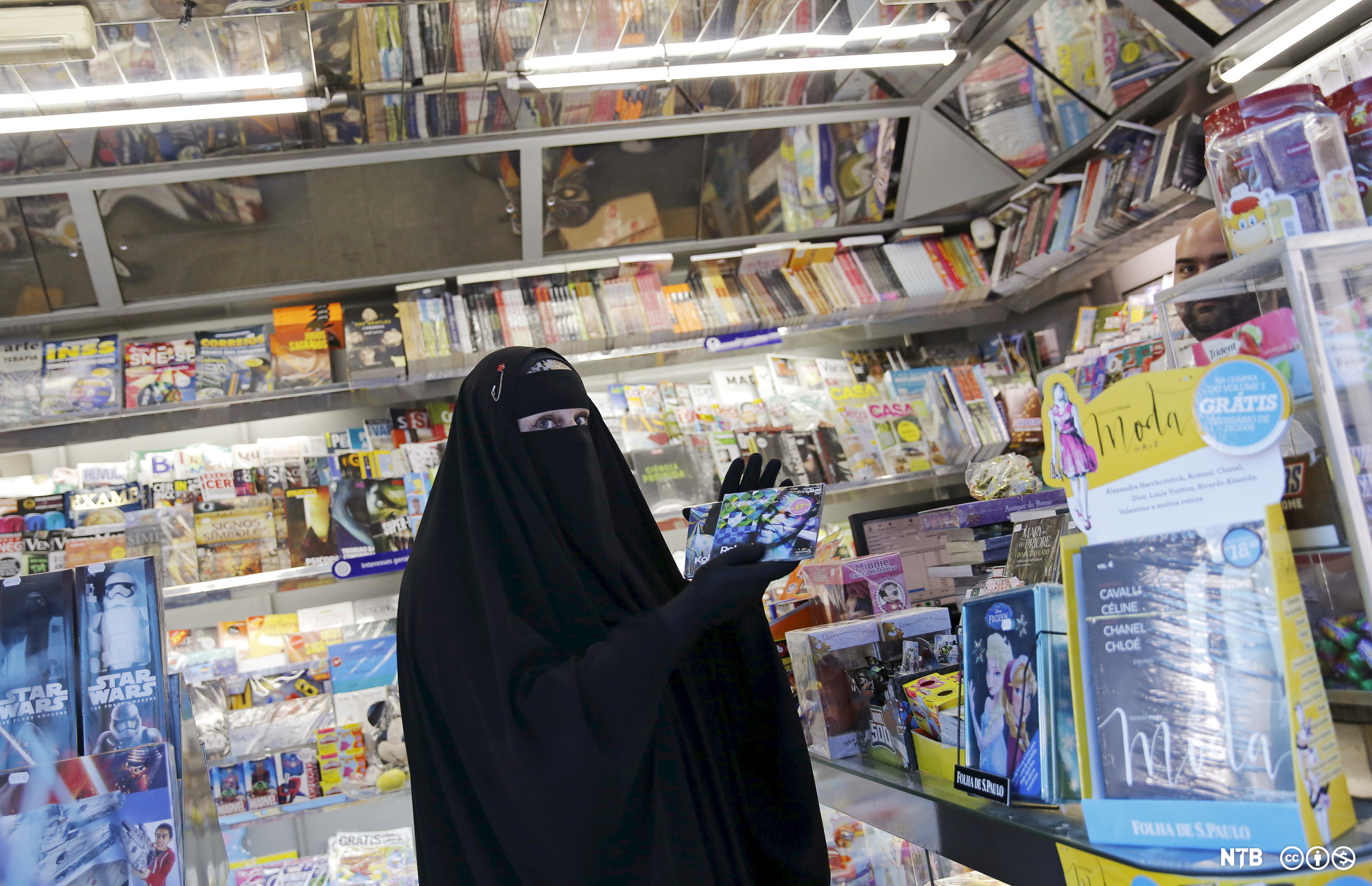 Kvinne med nikab og svart heldekkende drakt i en kiosk med magasiner og CD-plater. Foto.