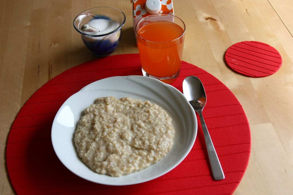 Hvit tallerken med havregrøt og et glass rød saft på bord med rød duk.