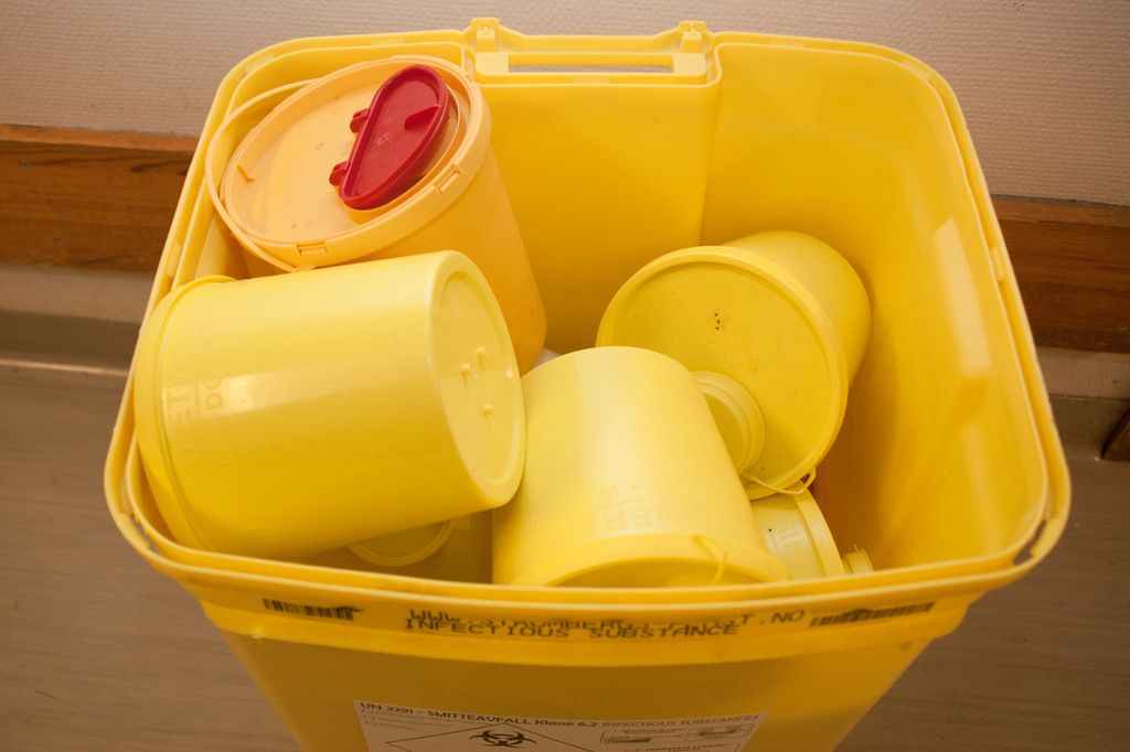 Gul søppeldunk med gule plastbokser for risikoavfall. Foto.
