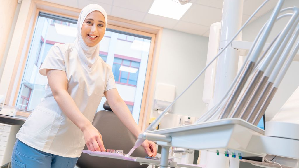 Kvinne i uniform for helsepersonell setter tannlegebrett på instrumentbord. Foto.