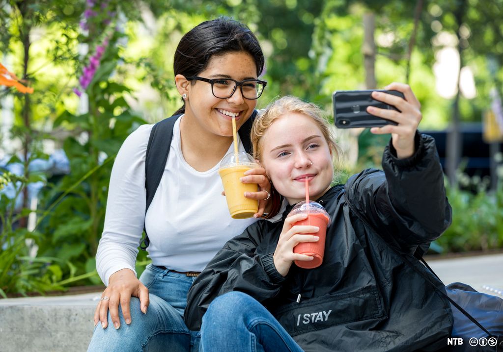 To jenter som drikk smoothie og tek selfie. Foto.  