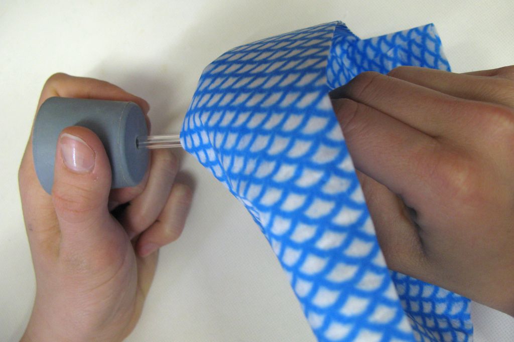 Ei hånd beskyttet av en klut fører et glassrør inn i en kork. Foto.