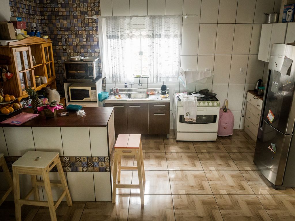Et stort kjøkken med fliser på veggene, kjøkkenøy, gasskomfyr, mikrobølgeovn, en ekstra elektrisk ovn, kjøkkenvask med enkel kum og kjøleskap. På kjøkkenøya er det masse frukt. Frontene på kjøkkenet er ulike: Noen har fliser, noen er mørkebrune, noen er hvite, og et overskap er av umalt treverk. Foto.