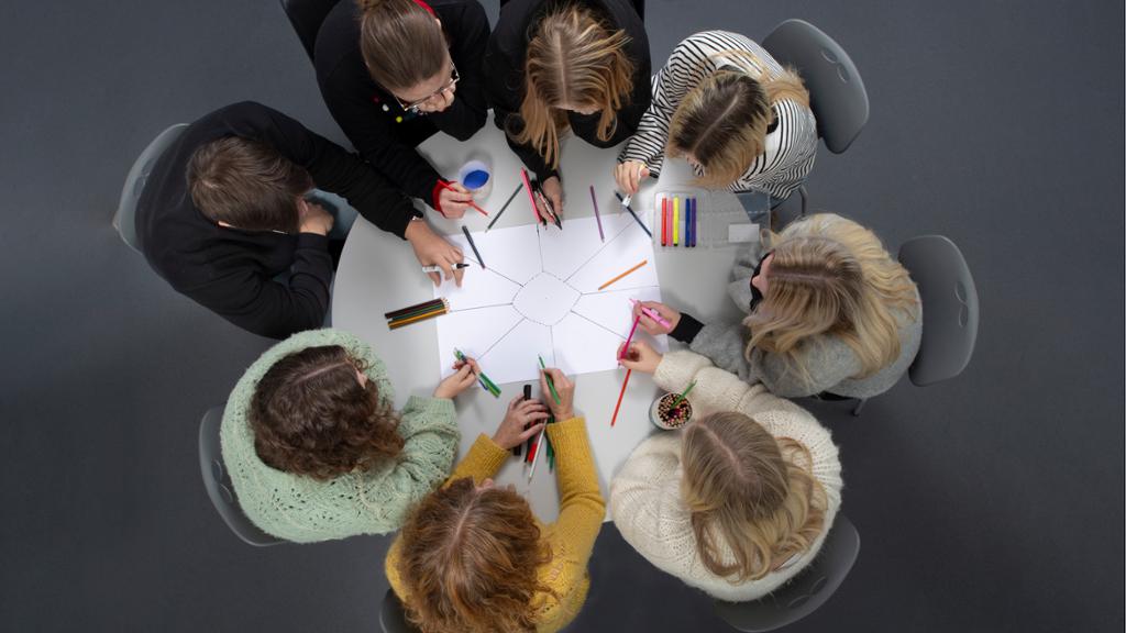 Åtte elever starter en idémyldringsprosess rundt et bord. Foto.