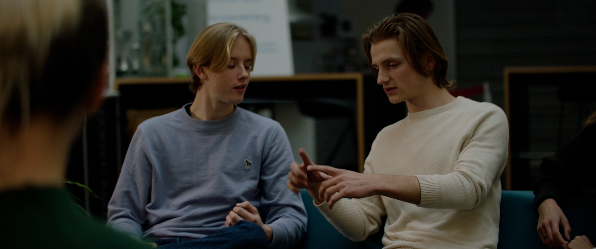 To unge gutter sitter og snakker. Den ene viser noe med hendene. Foto. 