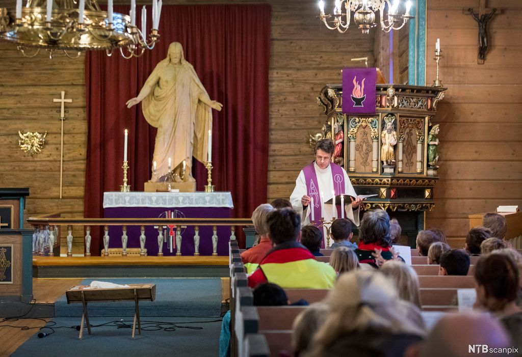 Prest tenner lys. Skoleelever sitter i kirkebenkene. Foto.
