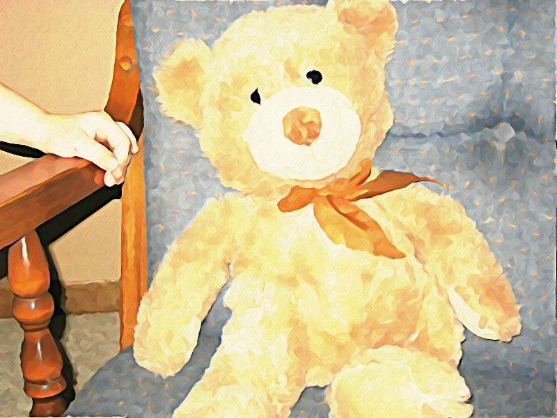 A yellow teddy bear with an orange bow is sitting in a chair. A child's hand is holding the armrest. Watercolour illustration. 