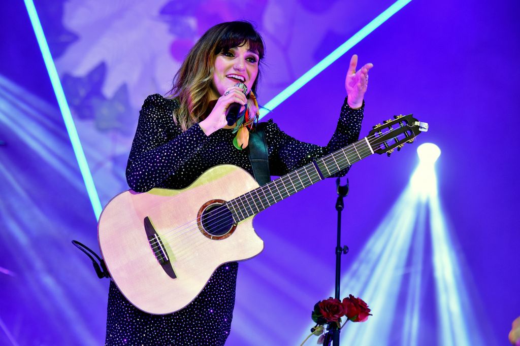 En kvinnelig artist med mikrofon og gitar på en scene. Foto.