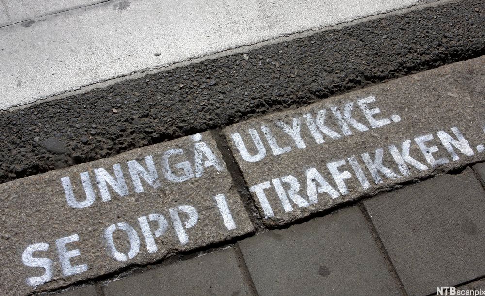 Fortauskant med påmalt tekst "Unngå ulykke" og "Se opp i trafikken". Foto.
