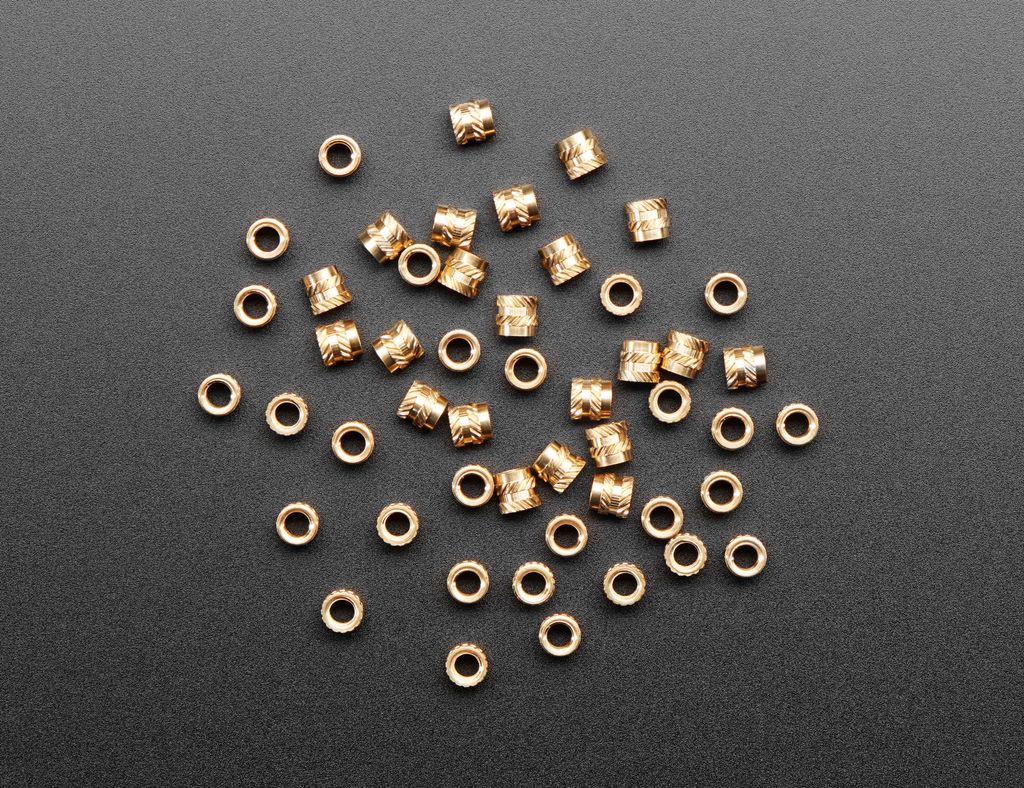 Mange sylinderforma deler med riller på utsida og gjenger inni ligger på ei plate. Foto.