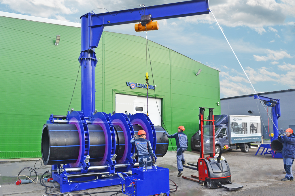 Et enormt plastrør montert i en maskin. Tre personer jobber med å få røret på plass. Foto.