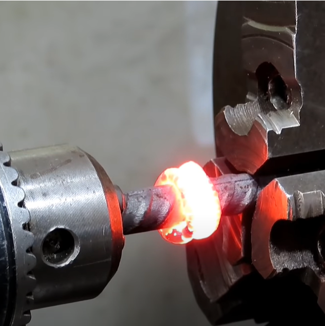 Glødende stålaksling mellom to mekaniske holdere. Foto.