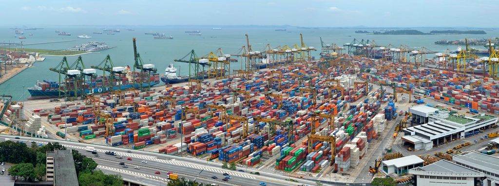 Stort oversiktsbilde av ei havn med enorme mengder konteinere i forgrunnen, store kraner ved vannkanten og havet i bakgrunnen. Foto. 