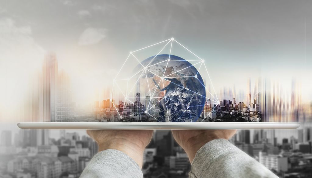 To hender balanserer et nettbrett horisontalt. Opp av nettbrettet stiger en jordklode omkranset av et nettverk av hvite, lyse striper. I bakgrunnen ser vi et skyskraperlandskap. Foto og digital illustrasjon.