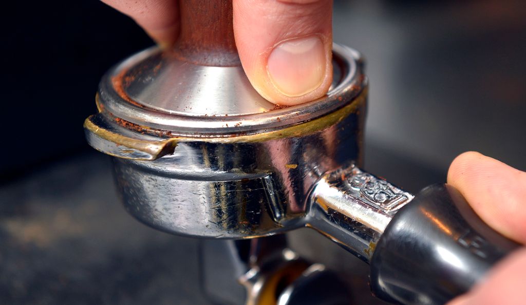 To hender pressar saman kaffi i ein filterhaldar. Foto.