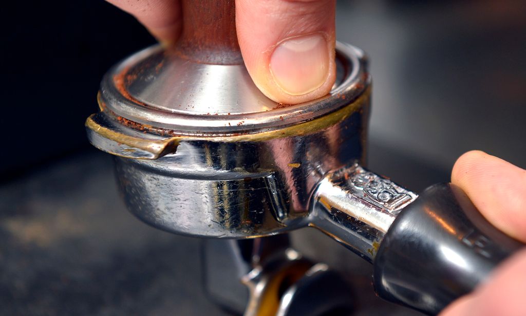 To hender presser sammen kaffe i en filterholder. Foto.