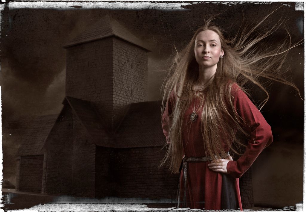 Ung kvinne med mørk rød kjole foran ei steinkirke med et høyt tårn. Kvinnens lange hår flagrer i vinden, hun holder hendene på hoftene og ser bestemt foran seg. Manipulert foto.