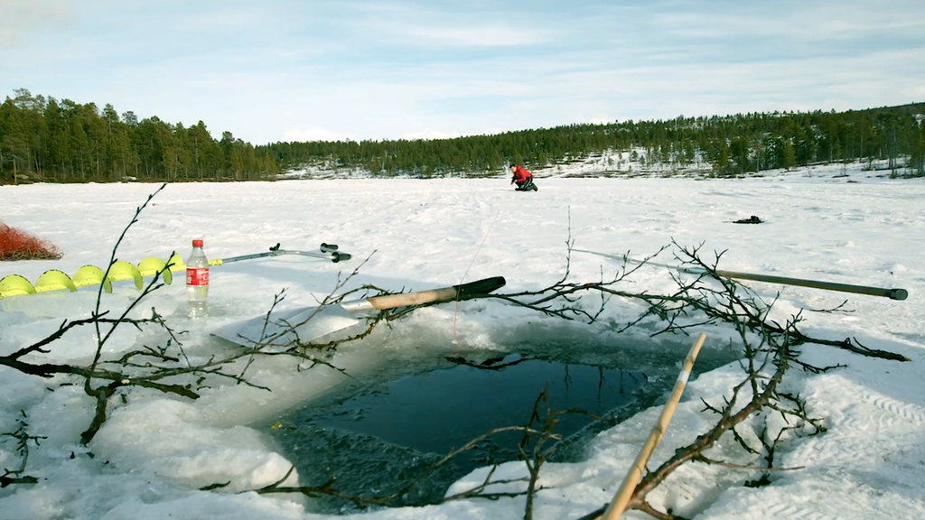 Hull i isen med en person i bakgrunnen. Foto.