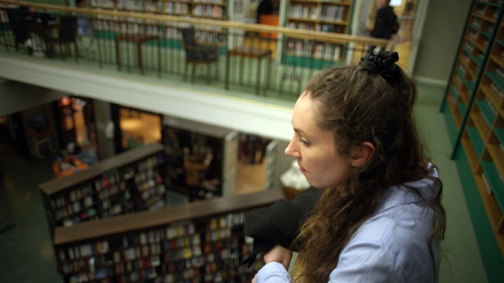 Kvinne som står og ser ned i atriet på et bibliotek. Foto.