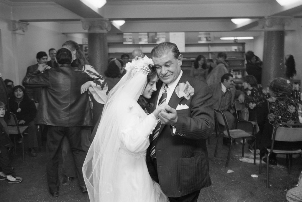 Far og datter danser sammen i et bryllup. Bruden har langt slør og hvit langermet kjole, far er i dress med bakoverkjemmet hår og blomst i knapphullet. Foto. 